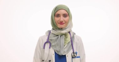 Başörtülü Müslüman kadın doktor beyaz arka planda gülümsüyor. Üniformalı kadın terapist, olumlu duyguları eşit fırsatlarla yansıtıyor.