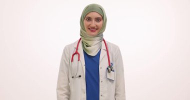 Başörtüsü takan kendine güvenen kadın doktor beyaz arka planda iyi bir jest gösteriyor. Steteskoplu neşeli Müslüman kadın klinikte onaylandığını ifade ediyor.