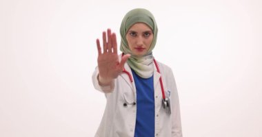 Tesettürlü Müslüman kadın doktor beyaz arka planda el hareketini durdurduğunu gösteriyor. Üniformalı kadın terapist klinik politikasına karşı olduğunu ifade etti
