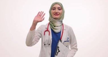Beyaz arka planda el yazısı tutan tesettürlü arkadaş canlısı kadın doktor. Üniformalı Müslüman kadın sıhhiyeci hastane randevusunda hastayı karşıladı