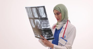 Başörtüsü konusunda kendine güvenen bir tıp uzmanı beyaz arka planda röntgen görüntüsünü inceliyor. Üniformalı Müslüman kadın bilgisayarlı tomografiden sonra hasta hastalığını inceliyor