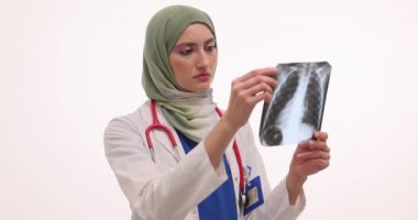 Tesettürlü kadın doktor beyaz arka planda hastanın göğüs röntgenini inceliyor. Müslüman kadın çalışmaları akciğer hastalığının teşhisi hakkında düşüncelere yol açıyor