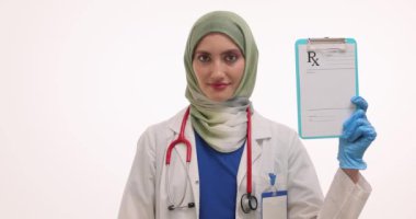 Kendine güvenen Müslüman doktor reçeteli olduğunu ve hapların bembeyaz olduğunu gösteriyor. Üniformalı kadın doktor hastalara sağlık hizmeti sunuyor