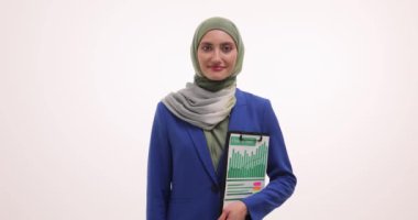 Tesettürlü Müslüman genç bir kadın, beyaz arka planla ilgili mali raporlarla dolu bir pano tutuyor. Gülümseyen bayan yönetici pozla kendine güven gösteriyor.