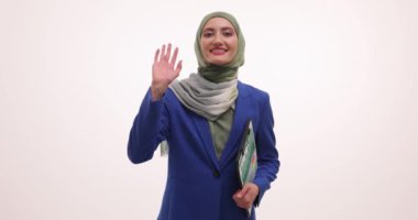 Tesettürlü Müslüman kadın beyaz arka planda müşteriyi selamlıyor. Dost canlısı bayan yöneticinin elinde müşteriyi karşılayan belgeler var.