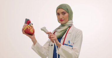 Türbanlı kadın doktor kalp modelini ve ultrason cihazını tutuyor. Müslüman kadın sıhhiyeci randevuda etkili ve müdahalesiz prosedürü açıkladı