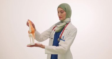 Başörtülü kadın doktor beyaz arka planda diz eklemi modeli gösteriyor. Steteskoplu Müslüman kadın doktor, yapısını gösteren öğrencileri eğitiyor