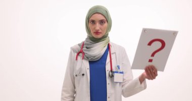 Tesettürlü kadın doktor beyaz üzerinde soru işareti olduğunu gösteriyor. Üniformalı Müslüman kadın doktor hastalara destek hizmeti sunuyor