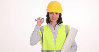 Sert şapkalı kadın mimar elinde beyaz üzerinde iyi bir jest gösteren planlar tutuyor. Gülümseyen bayan mühendislik kariyeriyle kendine güveni yansıtır