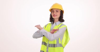 Kasklı ve yansıtıcı yelek giyen kadın mühendis beyazlara karşı kollarını kavuşturuyor. Üniformalı gülümseyen kadın işçi, kariyerine güvenini yansıtır.