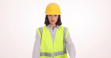 Güvenlik yeleği ve şapka takan üzgün kadın, beyaz arka planda durmayı gösteriyor. Kadın, ağır çekimde kollarını kavuşturmanın yasak olduğunu gösteriyor.