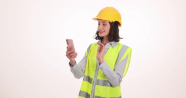 Yelekli ve kask takan kendine güvenen bir kadın telefonda video aracılığıyla konuşuyor. Üniformalı kadın mühendis çevrimiçi toplantı sırasında el sıkışma partneri