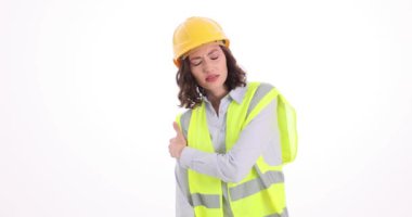 Güvenlik yeleği ve miğferi olan mimar kadın beyaz arka planda omzuna dokunuyor. Yaralı inşaat işçisi, acıyı tekrar yaşamak için masaj yapıyor.