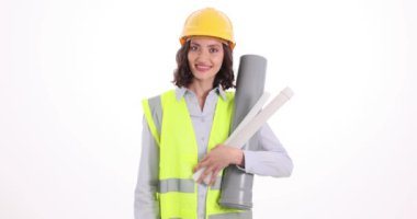 Çelik yelek ve çelik yelek giyen kadın mühendis, beyaz boru hattının planlarını ve bölümlerini elinde tutuyor. Kadın işçi kendine güvendiğini gösteren başparmak işareti yapıyor.