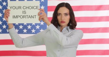 Kadınlar, Amerikan bayrağına karşı pankartla politik tercihlerin önemini hatırlatıyor. İş kadını insanları seçimlerde adaylara oy vermeye teşvik ediyor