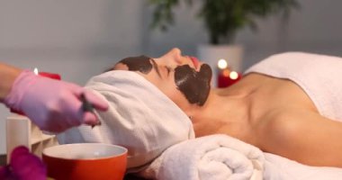 Kozmetik uzmanı kaplıcadaki kadının yüzüne gençleştirici siyah maske takıyor. Kil kavramından yapılmış kozmetik maskeler