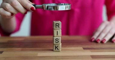 Kadın büyüteç kullanarak kelime riski olan tahta bloklara bakıyor. Ticari risk analizi yapıyoruz.