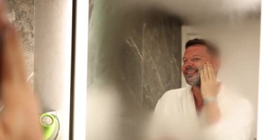 Mutlu gülümseyen yakışıklı adam sabahları aynanın önünde tıraş olmaya hazır. Erkekler için yüz bakımı