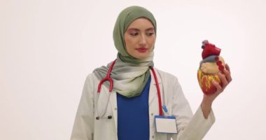 Türbanlı kadın kardiyolog, beyaz üzerinde kalp modeli gösteriyor. Ultrason cihazı olan Müslüman kadın doktor hastaya etkili bir prosedür sunuyor
