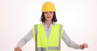 Güvenlik kaskı takmış üzgün bir kadın beyaz arka planda baş parmak hareketlerini gösteriyor. Kadın mühendis, inşaat projesiyle ilgili hayal kırıklığını yansıtıyor