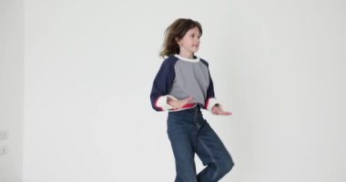 Yüzünde vitiligo izi olan küçük bir kız beyaz arka planda zıplayarak dans ediyor. Kot pantolon ve sweatshirt giyen çocuk hareketli bir hareket sergiliyor.