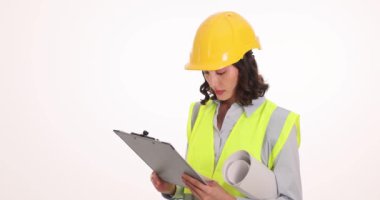 Meşgul kadın mühendis beyaz duvara karşı panoda gazete okuyor. Güvenlik kaskı ve yeleği olan genç bir kadın proje üzerinde çalışıyor.