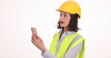 Kadın mühendis, partneriyle telefonda görüntülü sohbet yoluyla konuşuyor. Şapkalı ve üniformalı yetenekli genç bir kadın beyaz arka planda iletişim kuruyor.