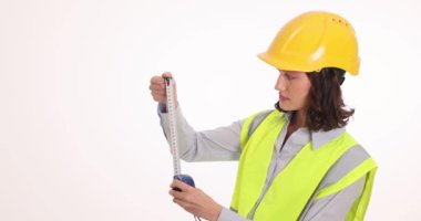 Kasketli kadın mimar, beyaz arka planda ölçüm bandı kullanıyor. Üniformalı kadın çalışan, gerekli aletlerle ölçümler yapıyor.