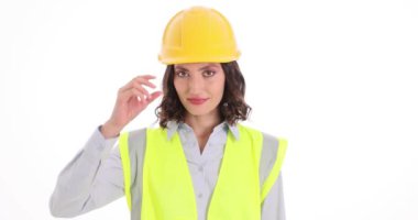 Güvenlik yeleği giymiş gülümseyen kadın mühendis beyaz arka plandaki işten sonra şapkayı çıkartıyor. Kendine güveni tam, genç, esmer, güzel gülüşlü bir kadın işçi.