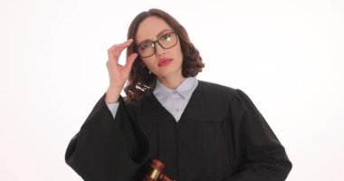 Kadın yargıç, beyaz arka planda şüphe uyandıran gözlükleri çıkarır. Kadın memur tokmak tutuyor. Duruşma sırasında tanık ifadelerini dinliyorlar.