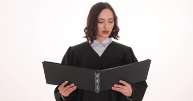 Önlüklü kadın yargıç beyaz arka plandaki yasal belgeleri okuyor. Konsantre kadın, mahkemede profesyonelliği gösteren mahkeme kararını açıkladı