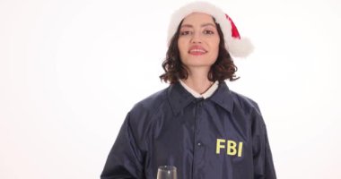 Noel Baba şapkalı kadın bir FBI ajanı beyaz arka planda şampanya kadehini kaldırıyor. Gülümseyen kadın memur partide mutlu Noeller diliyor.