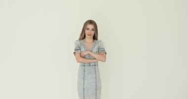 Gündelik elbiseli genç bir kadın beyaz arka planda kollarını kavuşturuyor. Kadın modeli şık portrede kendine güvenen ve ciddi bir ifade sergiliyor.