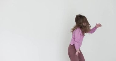 Neşeli genç kız beyaz arka planda dans edip zıplıyor. Gevşek saçlı enerjik liseli kız çocukluğunda yavaş çekimde kaygısız anların tadını çıkarıyor.