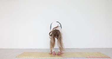 Genç bir kadın stüdyoda mindere basarak öne doğru eğiliyor. Günlük giysiler içinde gevşek saçlı bir kadın işten sonra yorgunluğu azaltmak için esneme egzersizi yapar.