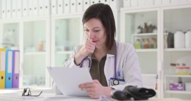 Steteskoplu kadın doktor klinikteki sağlık raporunu okuyor. Kadın profesyonel, endişeli yüz ifadesi olan hastanın tıbbi geçmişini inceliyor.