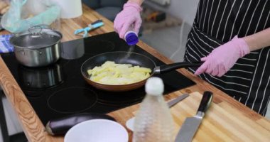 Çizgili önlüklü kadın evde fırında patates kızartması yapıyor. Steril eldivenli kadın aşçı akşam yemeği pişirirken tuzu dengeliyor.