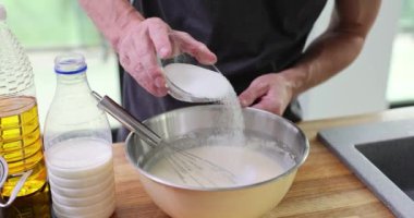 Adam kahvaltı hazırlamak için şeker çırpma malzemeleri ekliyor. Erkek aşçı, yerli mutfağın ahşap tezgahında krep hamuru hazırlıyor.