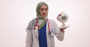 Kendine güvenen tesettürlü kadın doktor mankenle göz yuvarının anatomisini açıklıyor. Tesettür doktoru klinikte görselleştirmeyi kullanarak açıklama yapar