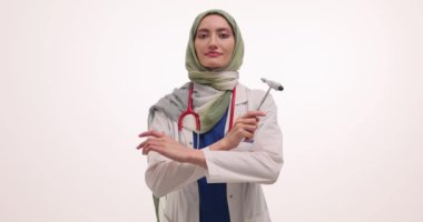 Müslüman kadın sağlık uzmanı tesettürde refleks çekici tutuyor. Üniformalı kadın doktor kendine güveni pozla yansıtır.