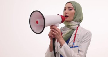 Kendine güvenen tesettürlü kadın doktor hastaya önemli bir mesaj iletmek için megafon kullanıyor. Üniformalı Müslüman kadın doktor ağır çekimde haberler bildirdi