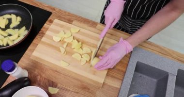 Kadın patatesleri tahta kesme tahtasıyla parçalara ayırıyor. Çizgili önlüklü kadın evde ağır çekimde lezzetli bir yemek için patates kızartması yapıyor.