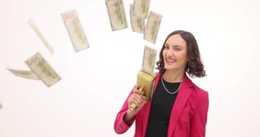 Pembe ceketli genç iş kadını beyaz arka planda para tabancasıyla para yağdırıyor. Bayan başlangıç projesinin finansal başarısını yavaş çekimde ifade ediyor
