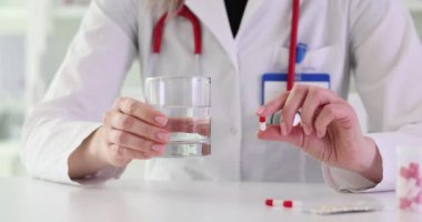 Beyaz önlüklü doktorun elinde kapsül ve bir bardak su var. Kadın terapist, sağlık ve tedavi için alınan ilaçları açıklıyor