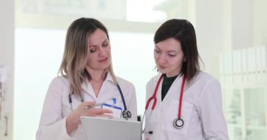 Kadın doktorlar hastanede evrakları panoda incelerler. Steteskoplu sırıtan sarışın ve esmer sağlık görevlileri hastaların tedavi sonuçlarını birlikte tartıştılar.