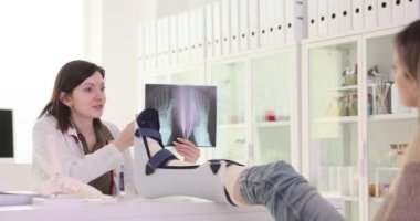 Doktor, alçıdaki kadına ayak röntgeni gösteriyor. Üniformalı kadın doktor, teşhis ve tedavi seçeneklerini açıklayan yaralanmayı tartışıyor