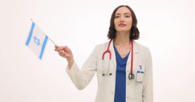 Mutlu kadın doktor beyaz arka planda İsrail bayrağı sallayarak gülüyor. Kadın terapist vatanseverliği ve gururu ülkede çalışarak yansıtıyor.
