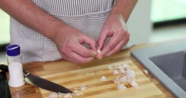 Önlüklü şef sarımsak karanfilini büyük tahta kesme tahtasında soyar. İnsan yemek için ilave malzeme olarak küçük bir tuz şişesinin yanında sarımsak soyar.