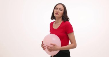 Genç bir kadın karnında ağrı hisseder ve beyaz arka planda balondan mideye bastırır. Kırmızı tişörtlü kadın keskin acıyı yavaş çekimde hafifletmeye çalışıyor.
