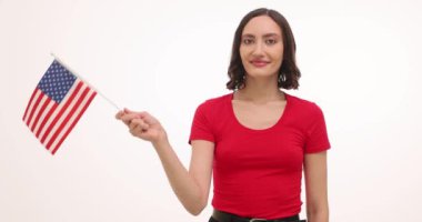 Kadın Amerikan bayrağı sallıyor ve beyaz arka planda ülkeye destek veriyor. Kadın, vatansever gururunu ve desteğini eşit haklara ağır çekimde aktarıyor.